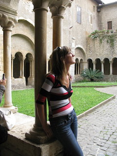 Woman leaning on stone column in medieval cloister with arched colonade and courtyard garden