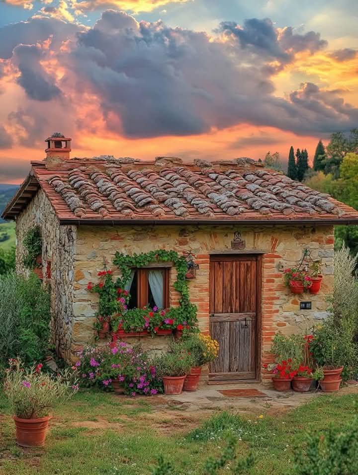 Stone cottage with flower pots at sunset with colorful clouds