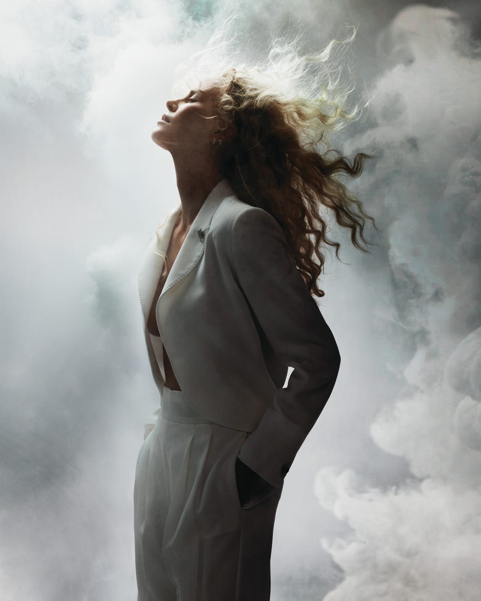 Woman in gray blazer suit with wild windswept hair against dramatic smoky cloud background