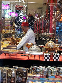 Vendor in red fez behind a market stall displaying Turkish sweets and ornate serving domes