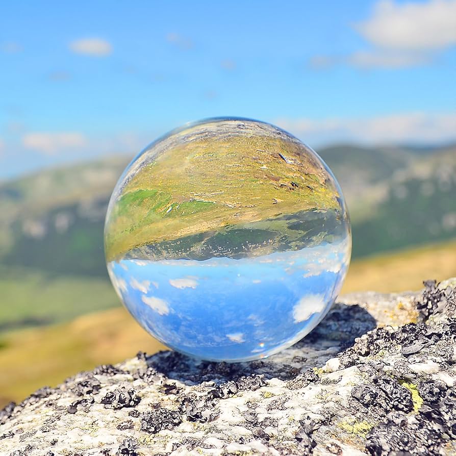 Glass crystal ball on a rock reflecting an inverted mountain landscape and blue sky