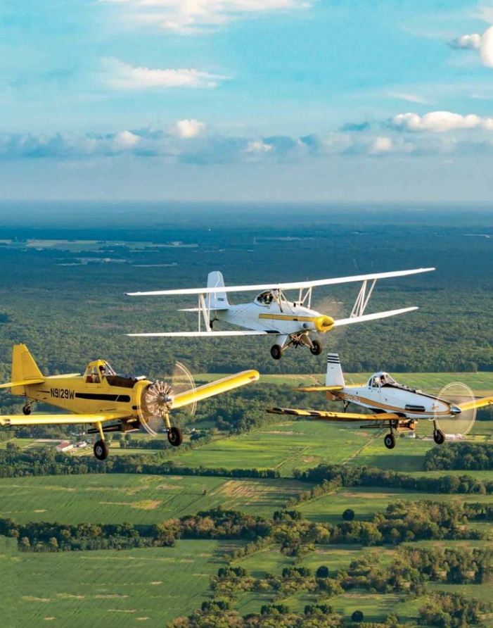Three crop duster aircraft flying in formation over green countryside with clouds above