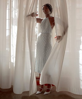 Woman in white halter dress and headwrap posing between sheer white curtains