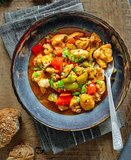 Bowl of chicken and vegetable stew with red peppers, zucchini, and mushrooms on a wooden table