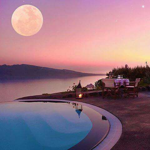 Infinity pool at dusk with ocean view and full moon in colorful sky