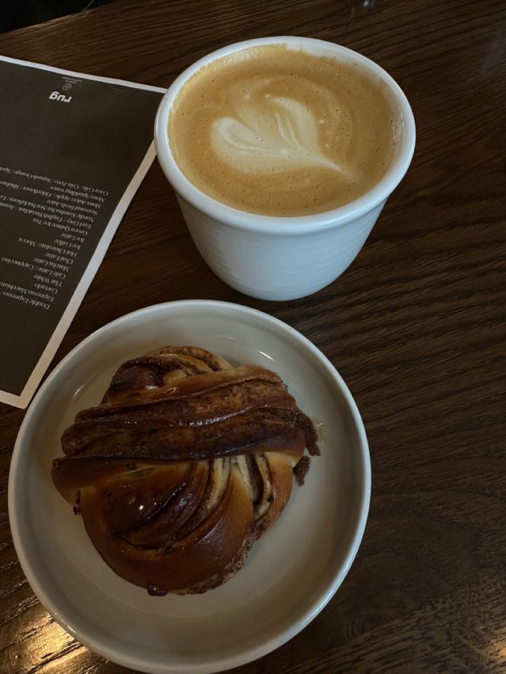 Cinnamon bun next to an oat milk latte in a glass cup