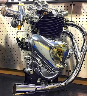Vintage Triumph motorcycle engine with chrome pipes and blue-silver finish mounted on pegboard