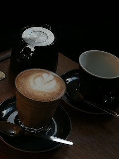 Latte with foam art on a dark table beside a black coffee pot and cup