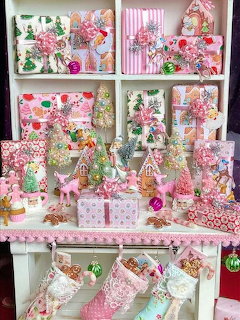 Vintage pink and white Christmas decorations arranged on white cabinet shelves with ornaments and miniature trees