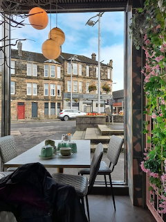 Cafe seating by a large window with a street view of stone buildings and parked cars