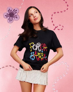 Young woman in black t-shirt and polka dot skirt posing against pink background with drawn flowers