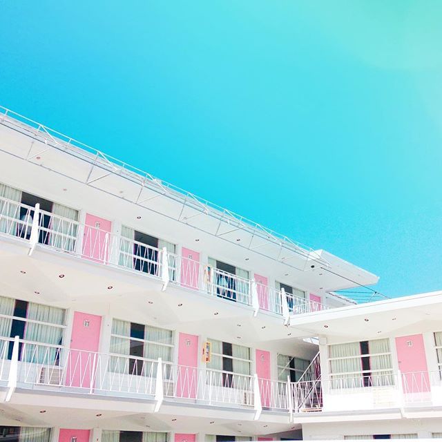 Pastel white motel with pink doors and balconies beneath a bright blue sky