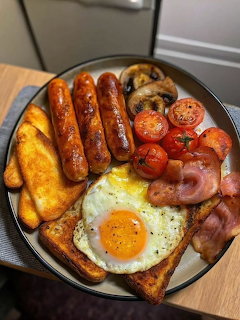 Cooked breakfast plate with sausages, fried egg on toast, bacon, tomatoes, mushrooms, and hash browns