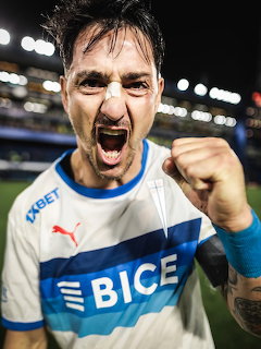 Soccer player in white and blue jersey celebrating with clenched fist and open mouth shout