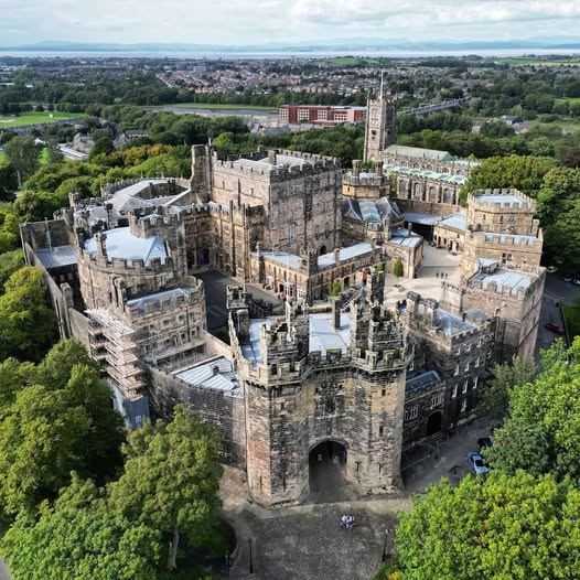 Aerial view of Lancaster Castle with stone towers, walls, and surrounding trees