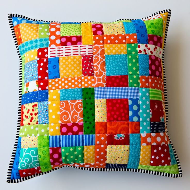 Colorful patchwork quilt pillow with polka dots, stripes, and floral fabric squares bordered with black and white trim