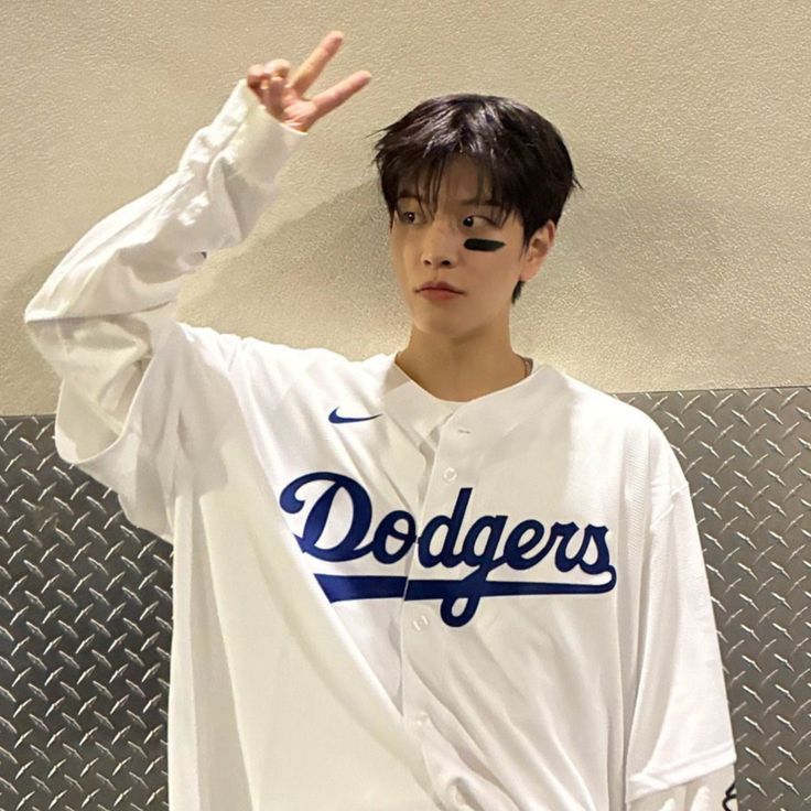 Person in white Dodgers jersey making peace sign against textured wall
