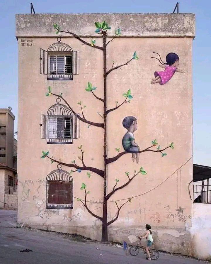 Street art mural of a tree with children and green birds painted on the side of a building