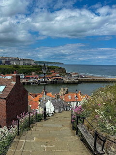 Stone steps descending through a seaside village toward a harbor and cliffs by the sea