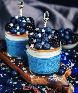 Two glass jars with blue layered dessert topped with blueberries and blackberries on wooden board