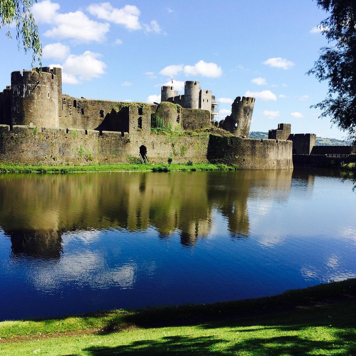 Caerphilly Castle reflected in moat water with blue sky and green grass