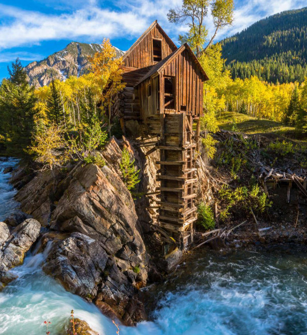 Crystal Mill wooden structure on rocky cliff above rushing river with autumn foliage and mountains