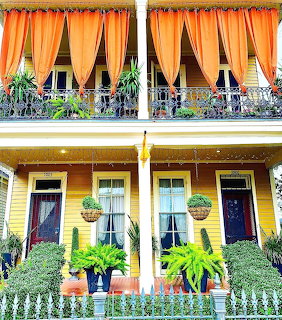 Colorful house facade with orange curtains, yellow walls, decorative balcony, and potted plants on porch