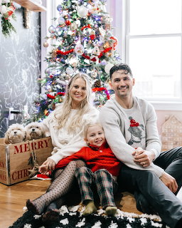 Family with two children and dog sitting by Christmas tree in white living room