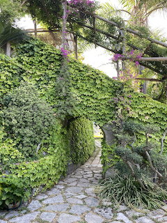 Stone path leading through an ivy-covered archway surrounded by lush green vegetation and wooden pergola