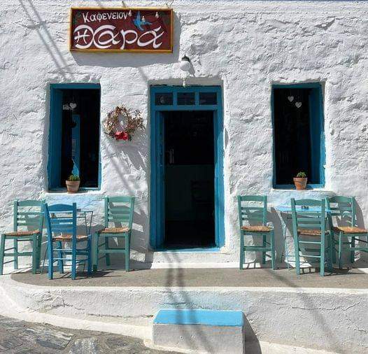 Traditional Greek café with blue doors, windows and wooden chairs against white wall