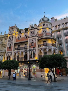 Ornate historic building in Seville with domed corner turret illuminated at dusk with trees in foreground
