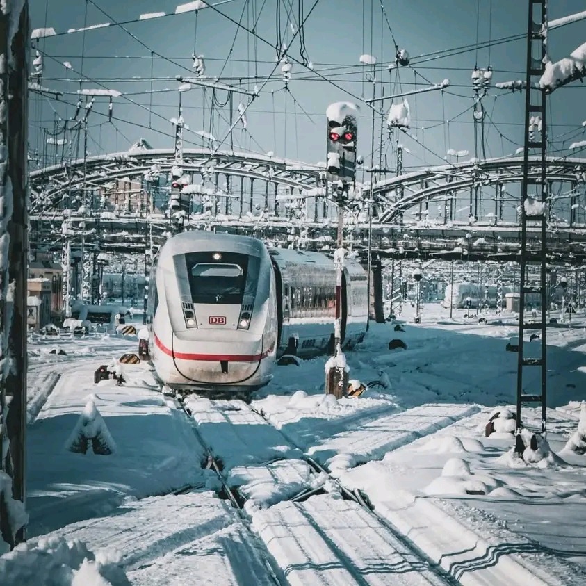 White high-speed train at snowy station platform with overhead wires