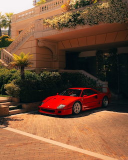 Red Ferrari F40 sports car parked outside a luxury building with stone facade and plants