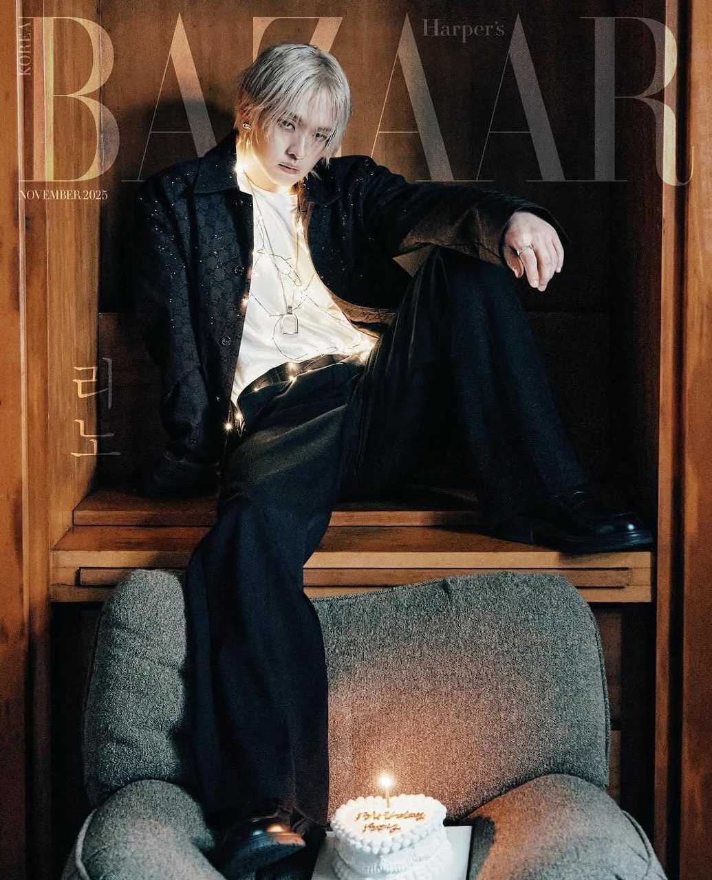 Young man with platinum hair in black jacket seated on Harper's Bazaar magazine cover with small cake