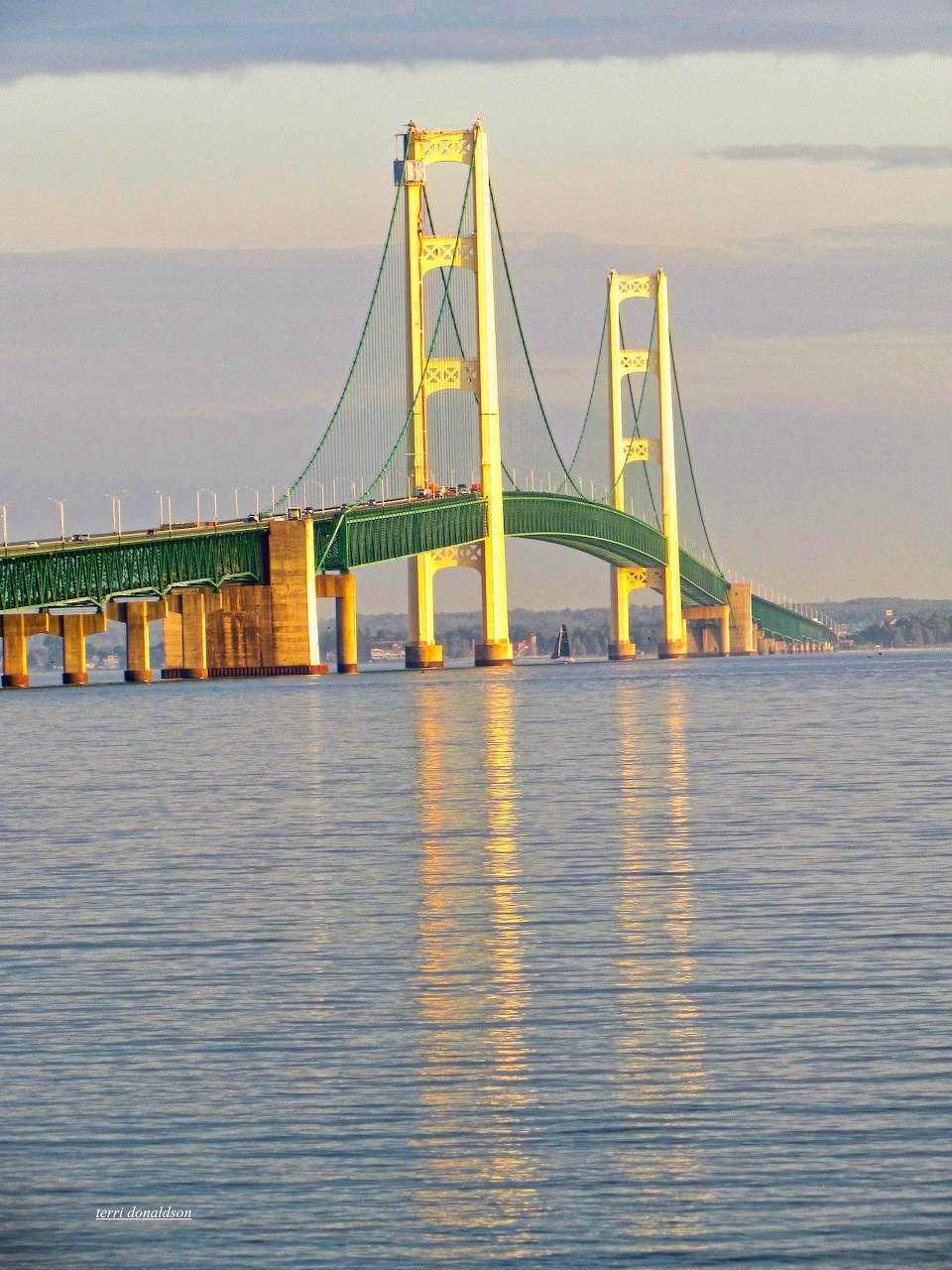 Suspension bridge over calm water with golden towers and reflections at dusk