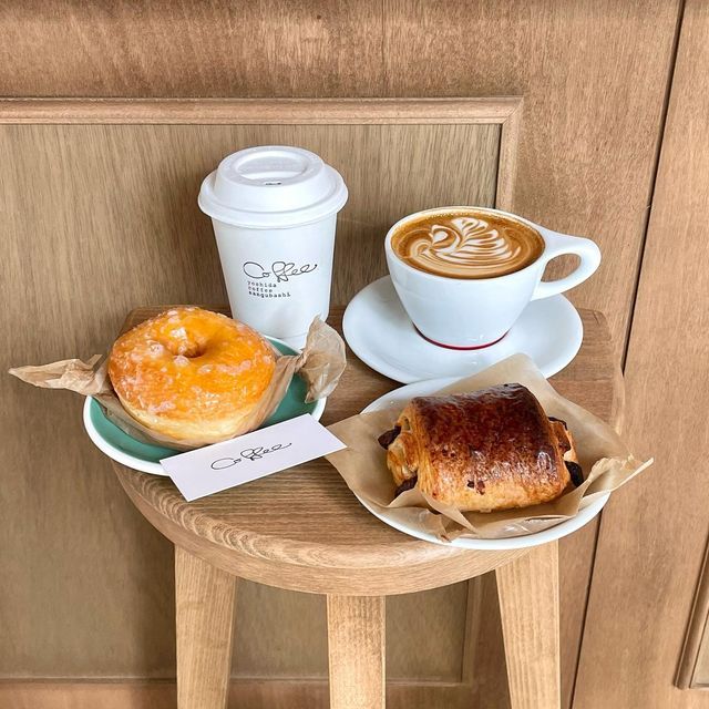 Coffee cup with swan latte art, takeaway cup, donut and chocolate croissant on wooden tray