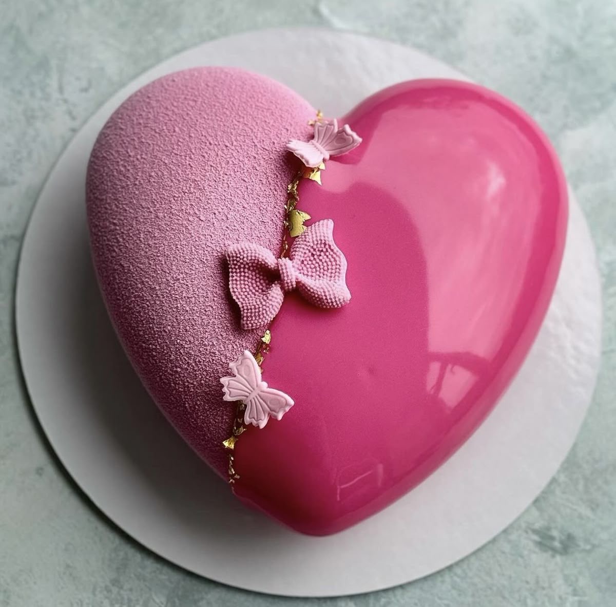Pink heart-shaped cake with glossy glaze, textured half, and butterfly decorations