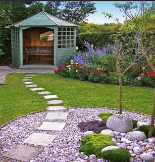 Green garden shed surrounded by flowering plants and stone path in a landscaped backyard