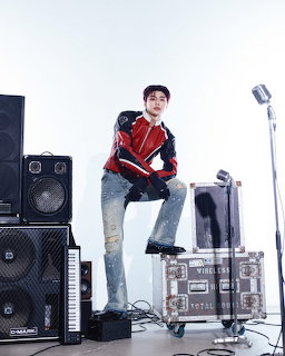 Young man in a red jacket posing with speakers, equipment cases, and a microphone in a studio