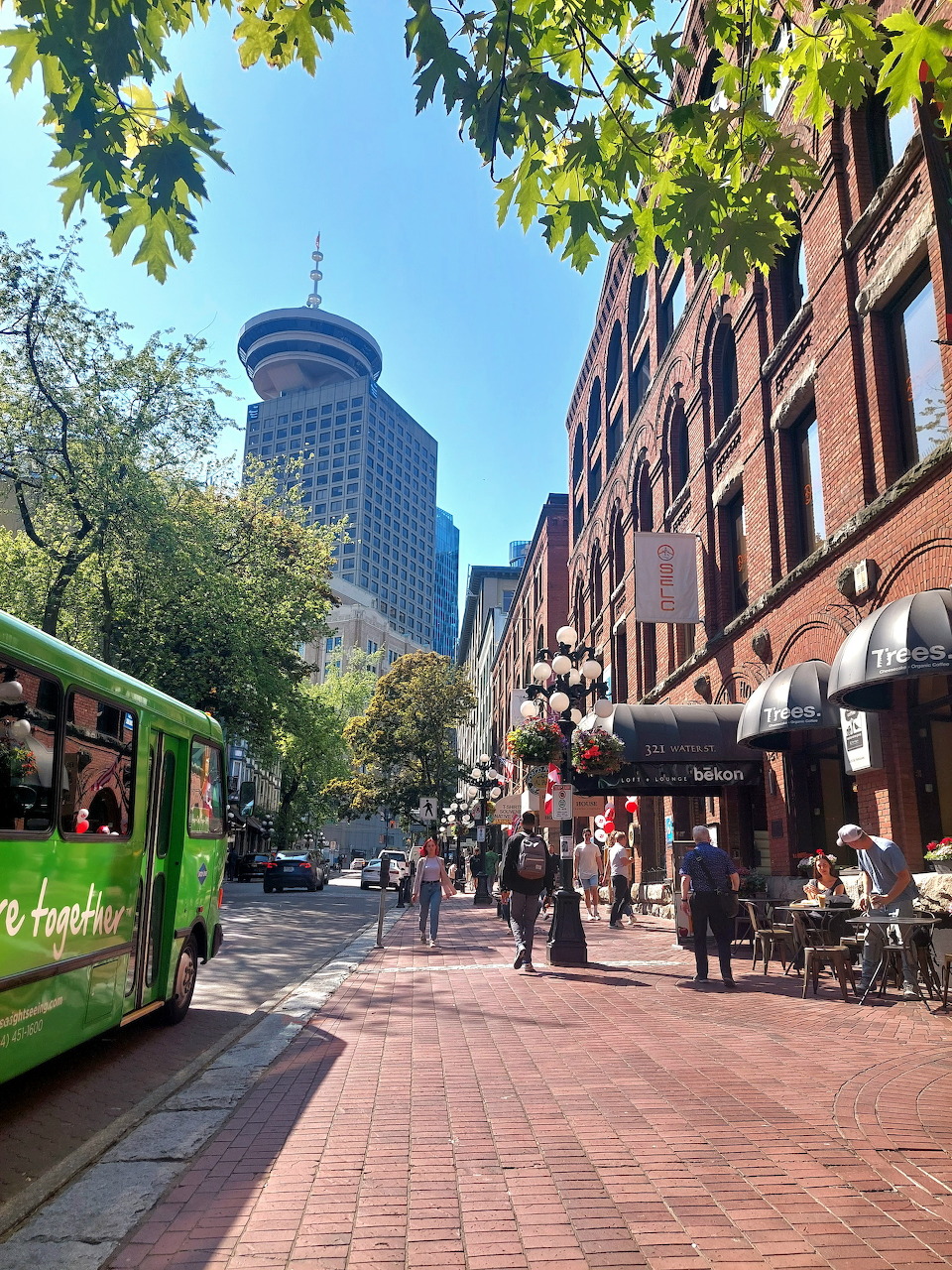 Downtown Vancouver street with brick buildings, trees, pedestrians, and a green trolley bus