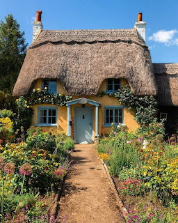 Yellow thatched cottage with blue door and windows framed by vibrant flower garden and stone pathway