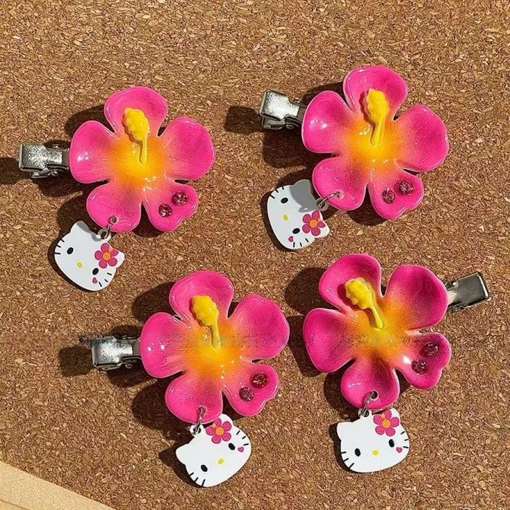 Four pink flower hair clips with Hello Kitty charms arranged on cork surface