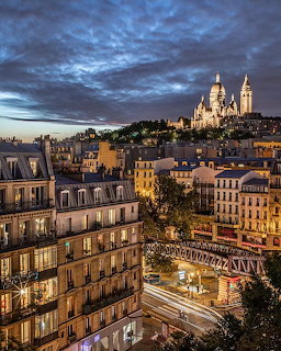 Parisian buildings and rooftops at dusk with illuminated Sacré-Cœur basilica on Montmartre hill