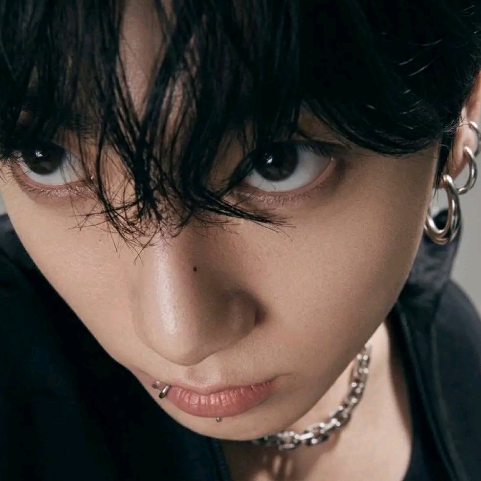 Close-up portrait of a person with black hair, earrings, lip piercing, and chain necklace