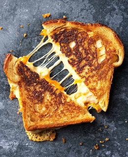 Grilled cheese sandwich with melted cheese pull on dark slate background