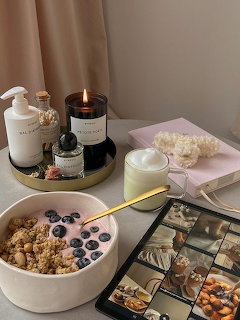 Breakfast bowl with granola, yogurt, and blueberries on a cozy table setting with tea and candles