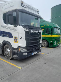 White Scania truck parked beside a green truck in an industrial yard