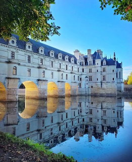 Château de Chenonceau castle with arched bridge reflected in river water surrounded by trees