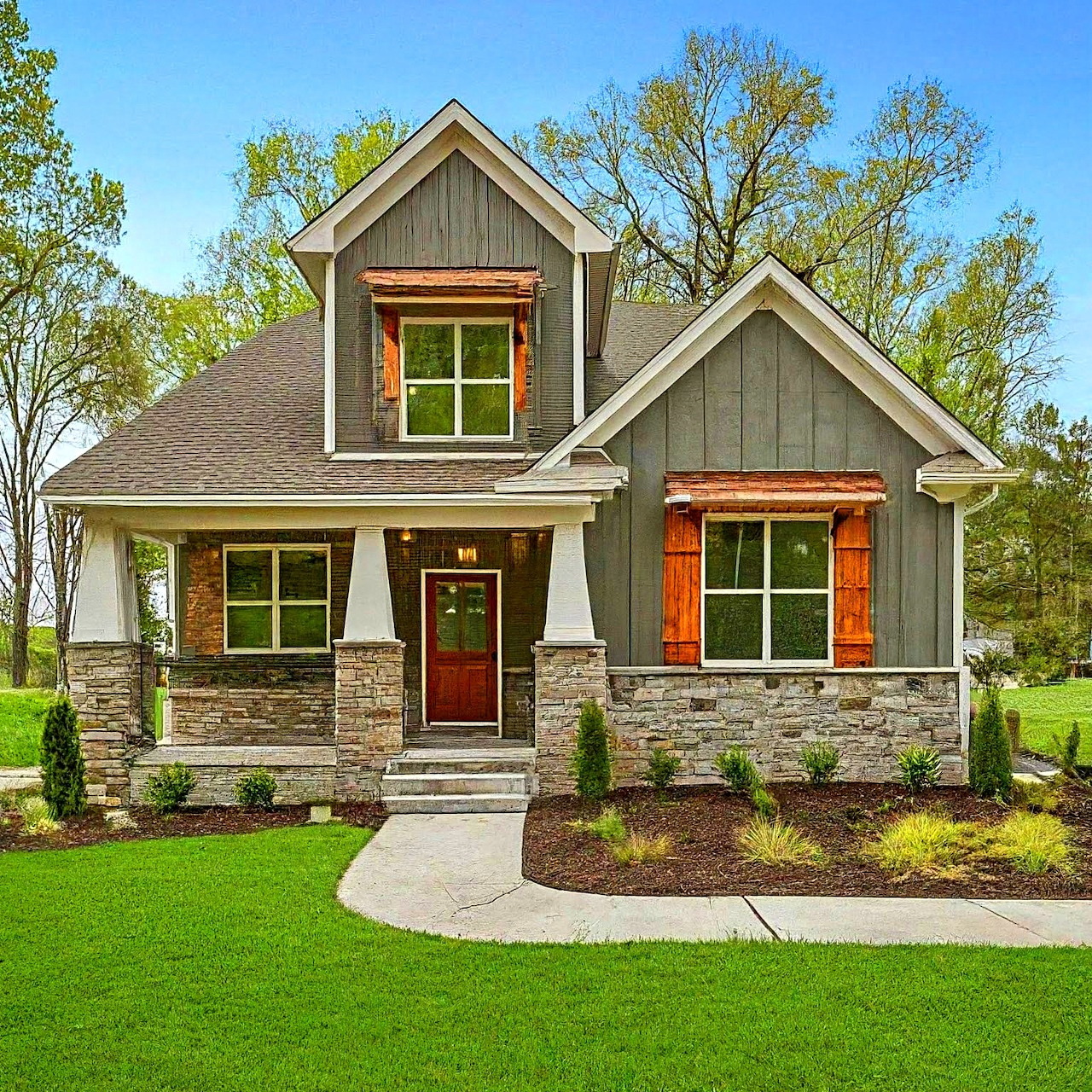 Craftsman-style gray house with stone columns, wood shutters, and a curved walkway across a green lawn