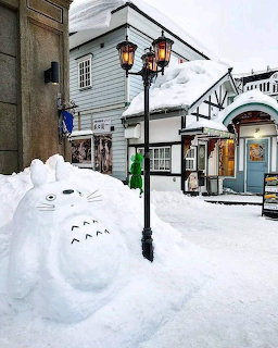 Large white Totoro snowman in snowy street with traditional Japanese buildings and street lamp